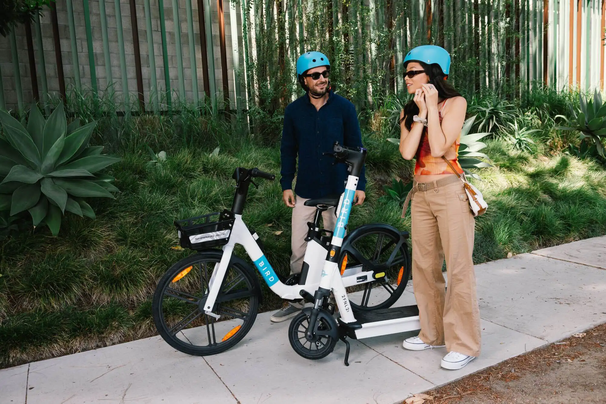 Dos personas de pie junto a una bicicleta eléctrica Bird en un sendero soleado